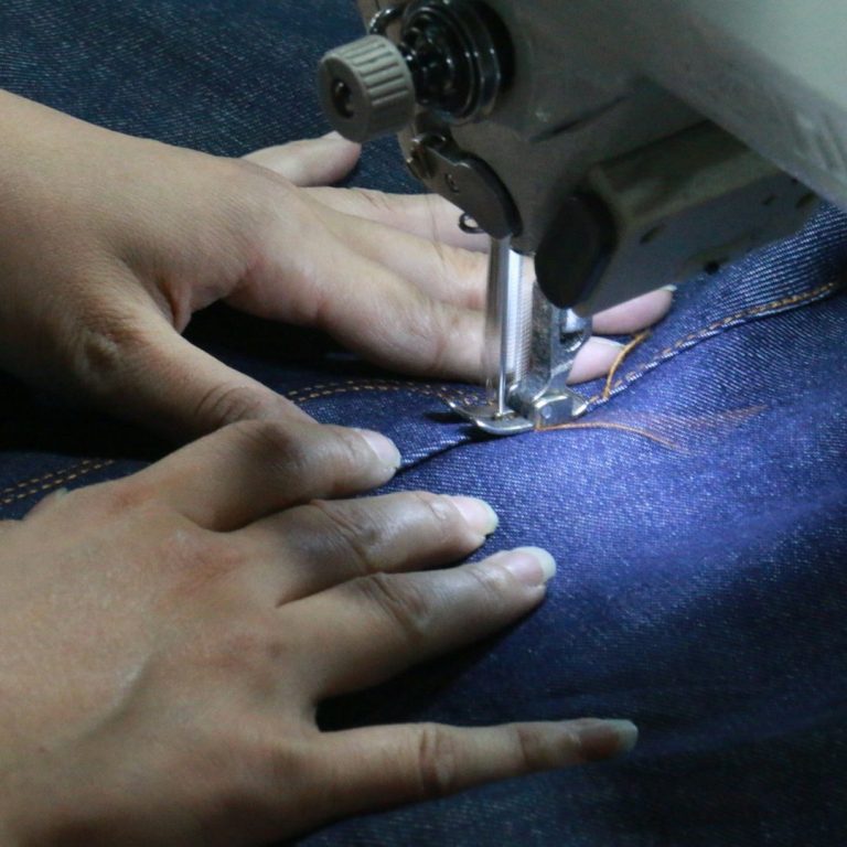 Herstellung einer Jeanstasche Hände nähen eine Jeanstasche mit einer Nähmaschine, Faden zieht durch den Stoff.