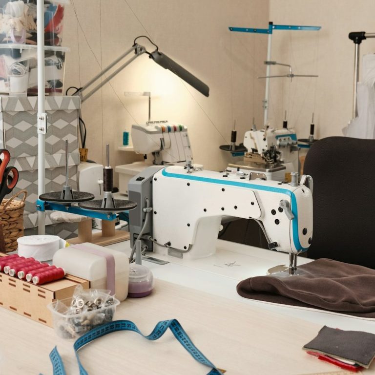 Nähmaschine und Zubehör auf einem Tisch, umgeben von Stoffen und Werkzeugen.